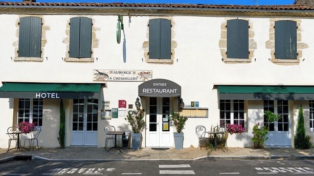 A building with a sign for a hotel and a restaurant. There are outdoor seating areas with tables and chairs. - Auberge La Crémaillère (Villandraut)