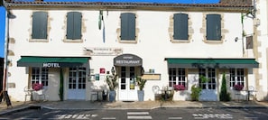 A building with a sign for a hotel and a restaurant. There are outdoor seating areas with tables and chairs. - Auberge La Crémaillère (Villandraut)