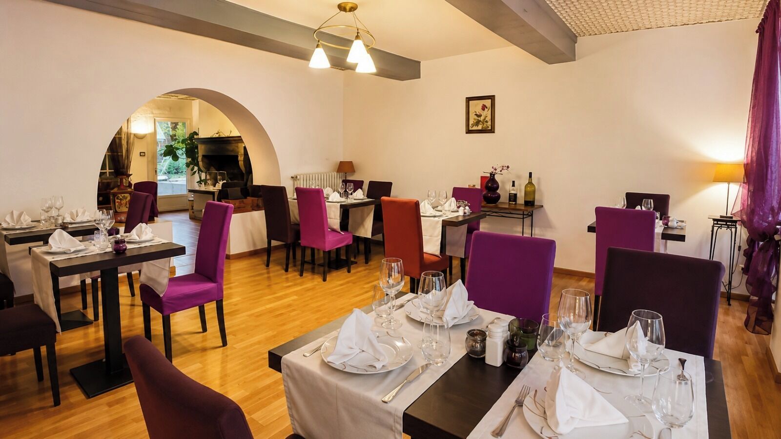 Un restaurante con varias mesas dispuestas para comer, sillas moradas y una chimenea al fondo.
