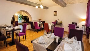 A restaurant with multiple tables set for dining, purple chairs, and a fireplace in the background. - Auberge La Crémaillère (Villandraut)