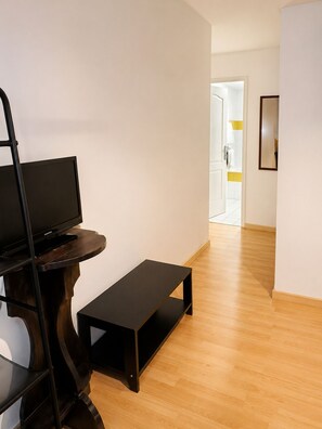 A room with a television on a stand, a small bench, and a door leading to a bathroom. - Auberge La Crémaillère (Villandraut)