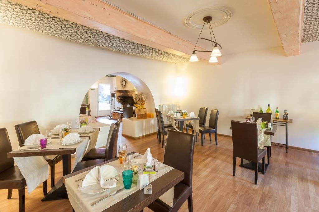 A dining area with tables set for guests, a kitchen in the background, and a wooden ceiling.