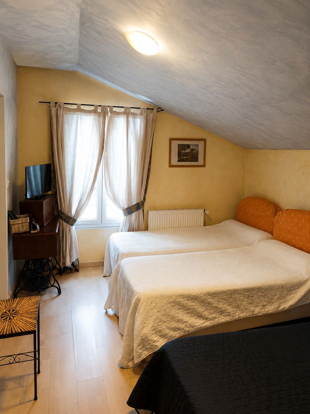 Una habitación con dos camas, un televisor sobre un mueble, un radiador y una ventana con cortinas.