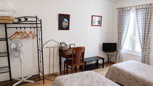 A room with two beds, a desk with a chair, a TV, a fan, and a window with curtains. - Auberge La Crémaillère (Villandraut)