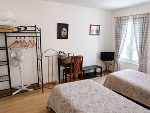 Una habitación con dos camas, un escritorio con silla, un televisor, un ventilador y una ventana con cortinas.