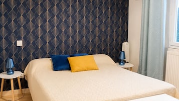 A bedroom with a bed, bedside tables, a bench, a patterned wall, and a window with curtains.