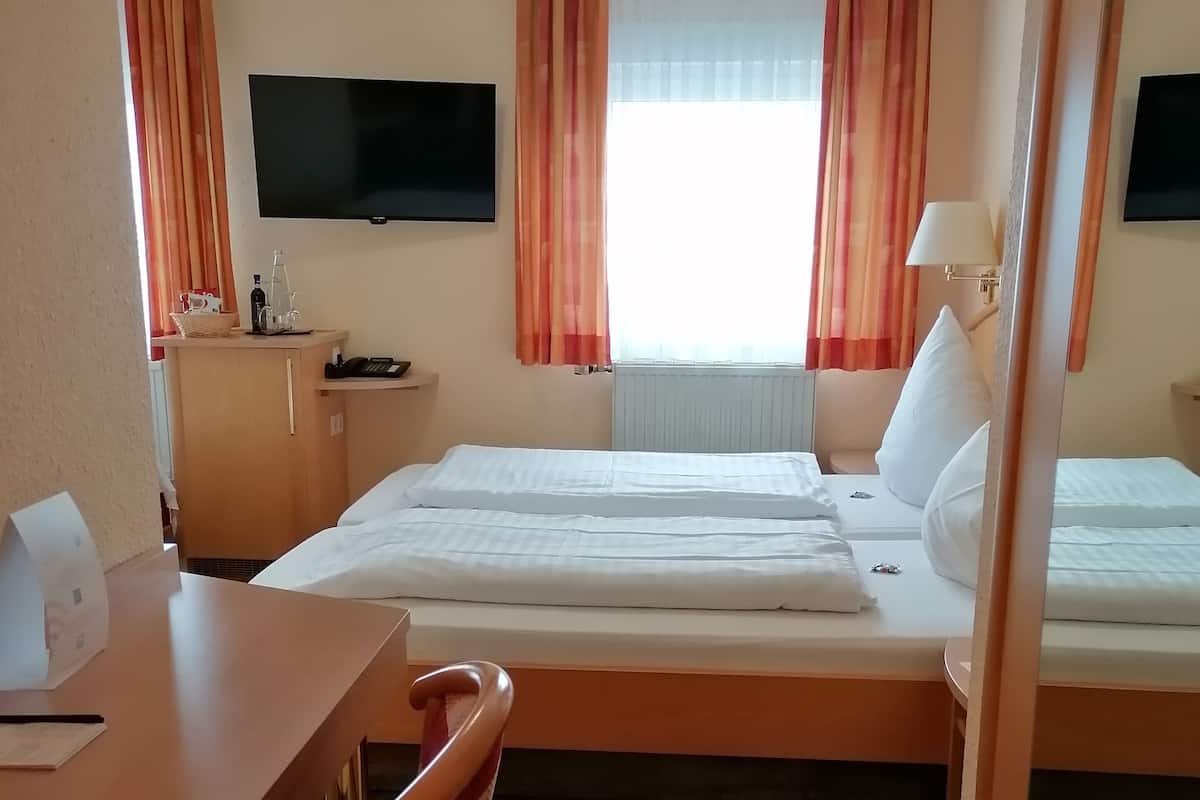 Een hotelkamer met twee bedden, een bureau, een stoel, een televisie en een raam met gordijnen.