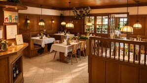 A restaurant with wooden interiors, tables set with white tablecloths, and hanging pendant lights. - Landgasthof Niebler (Adelsdorf)