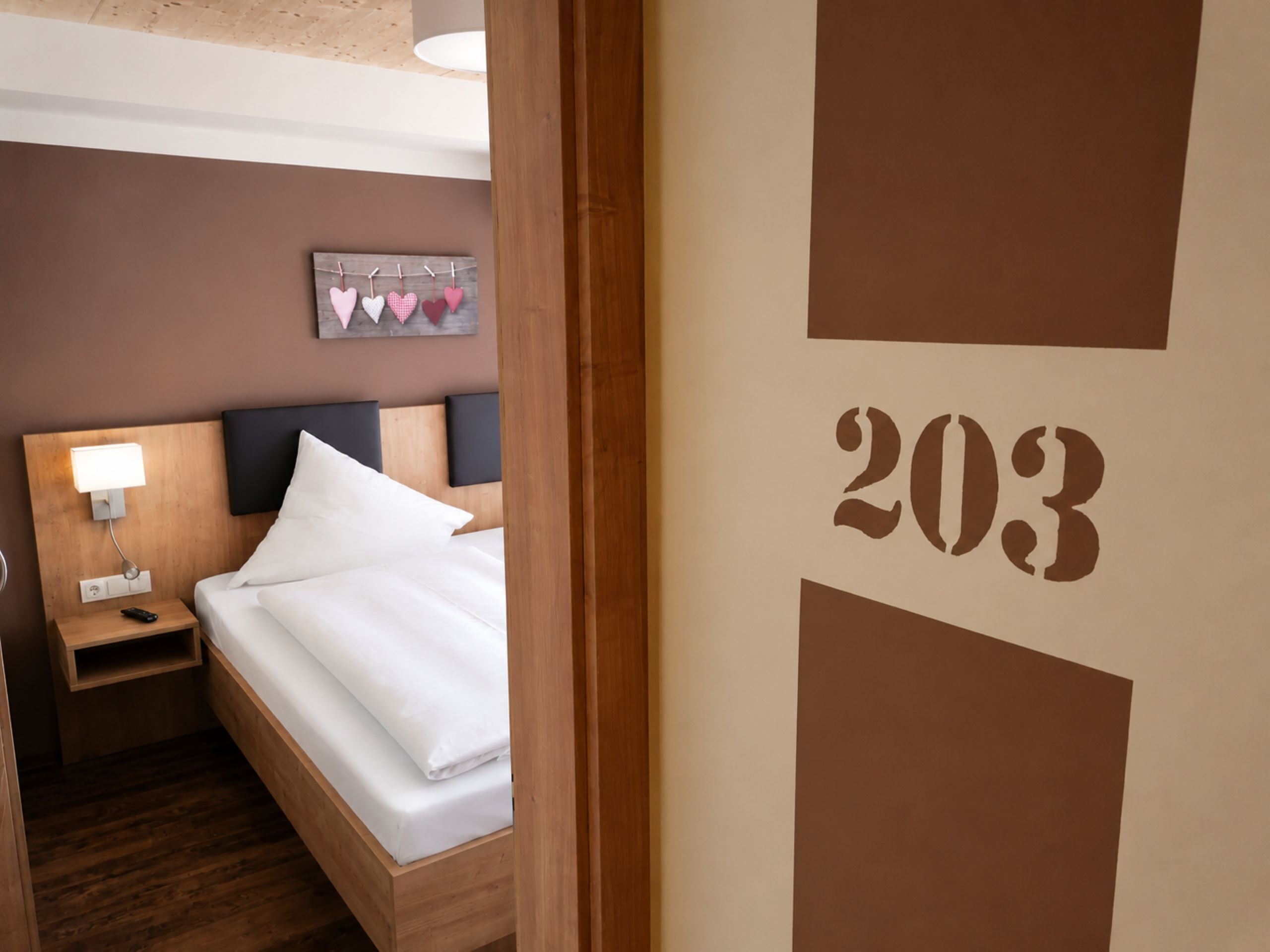 Hotellihuone, jossa on sänky, yöpöytä, lamppu ja seinä, jossa on numero 203.