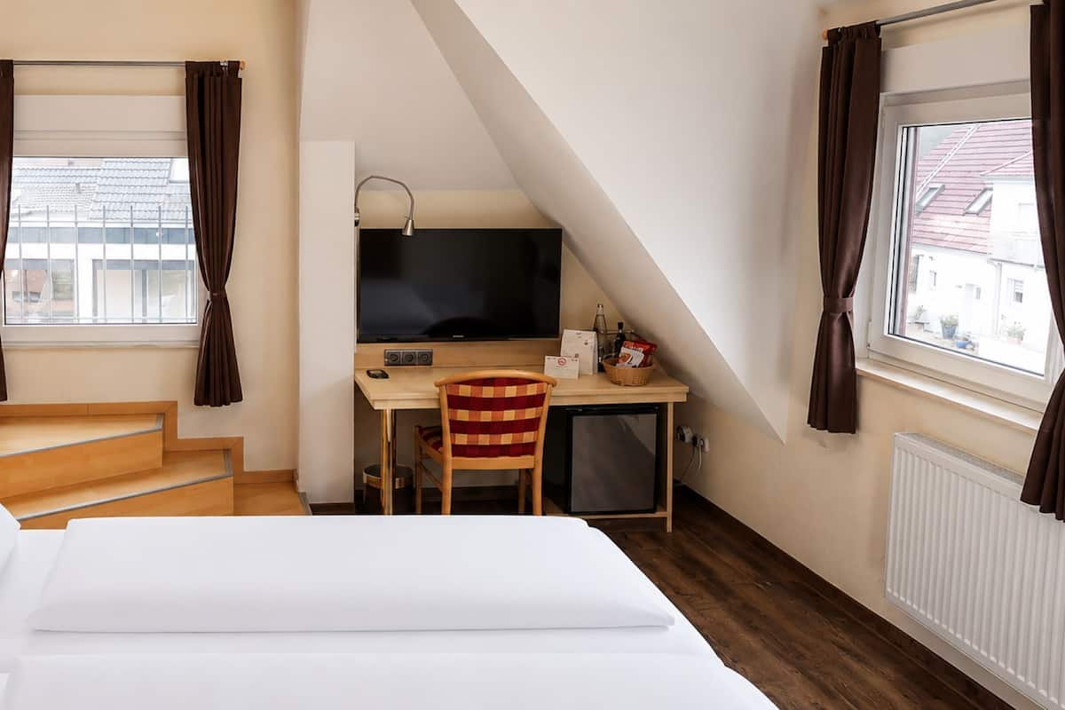 Een hotelkamer met een bed, een bureau met een computer, een stoel, een televisie en een raam met gordijnen.
