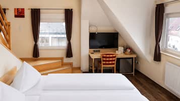 Ett hotellrum med en säng, ett skrivbord med en dator, en stol, en tv och ett fönster med gardiner.