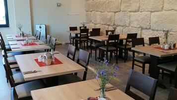 Un restaurante con varias mesas, cada una con manteles individuales rojos, teteras blancas y jarrones con flores. Las paredes presentan un diseño de piedra, y el techo tiene luces circulares.