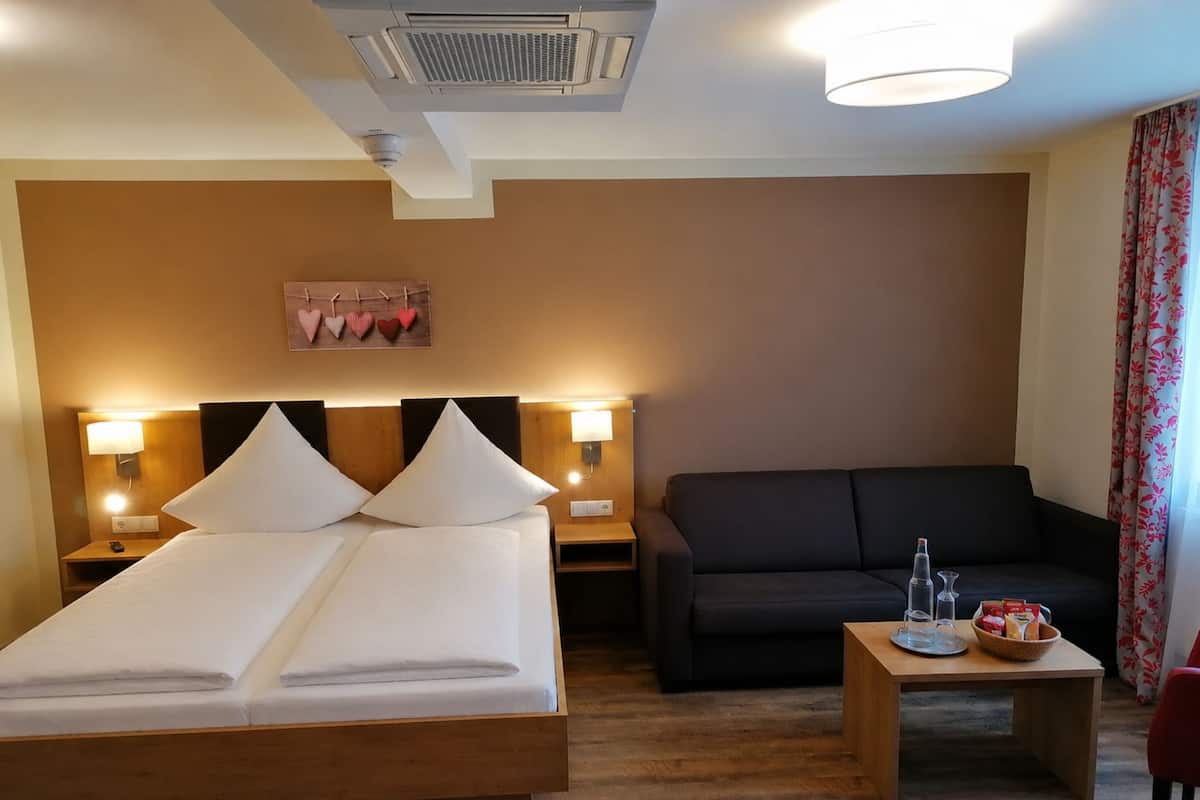 Een hotelkamer met een bed, een slaapbank, een klein tafeltje met glazen en hapjes, en een wandairconditioner.