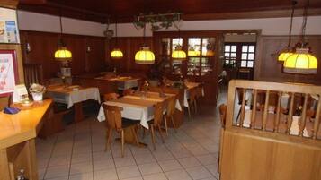 A restaurant with wooden tables and chairs, hanging lamps, and a tiled floor.