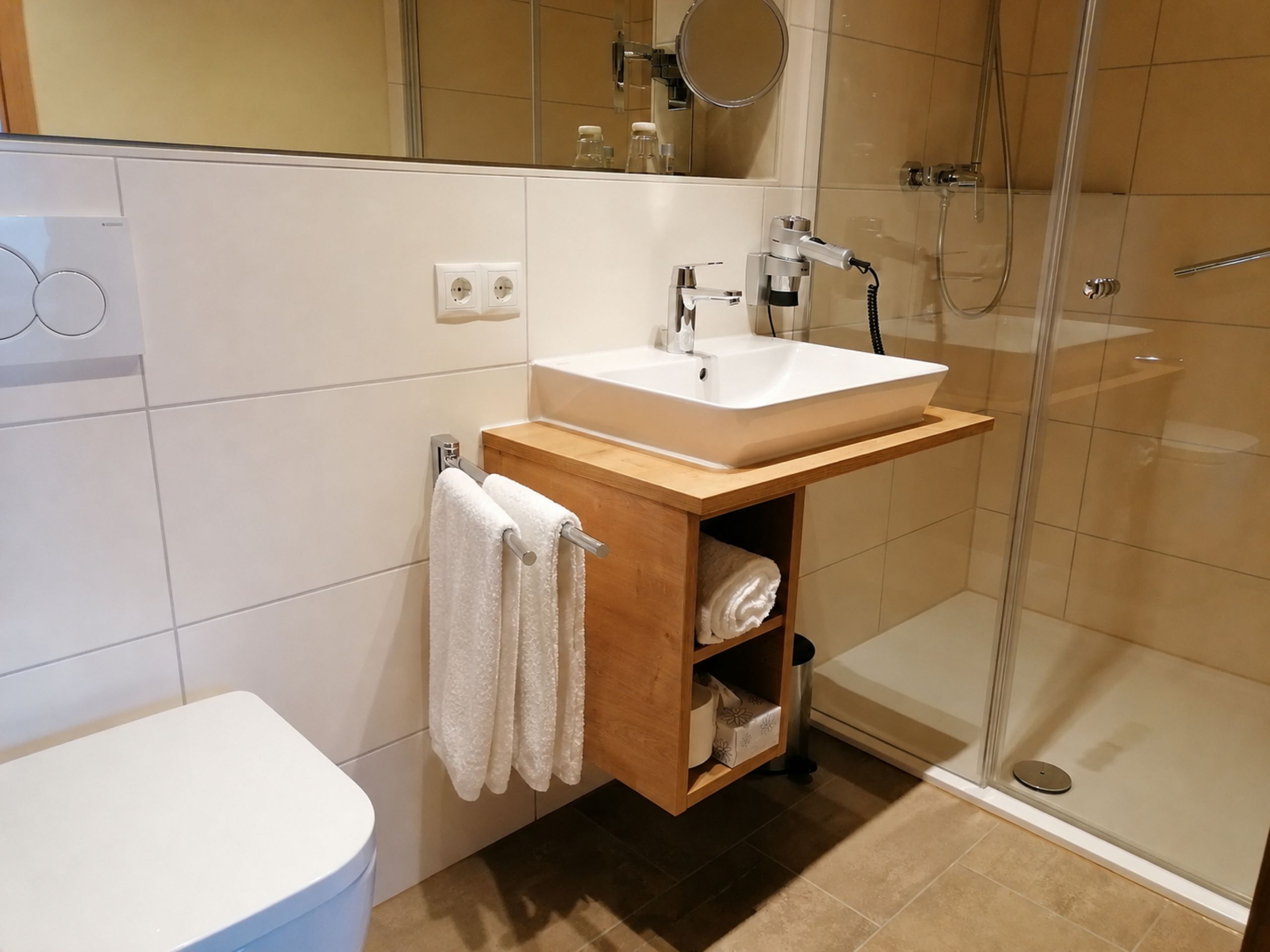 A modern bathroom with a white toilet, a wooden vanity with a sink, and a glass shower enclosure.