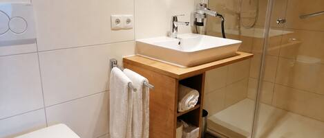 A modern bathroom with a white toilet, a wooden vanity with a sink, and a glass shower enclosure.