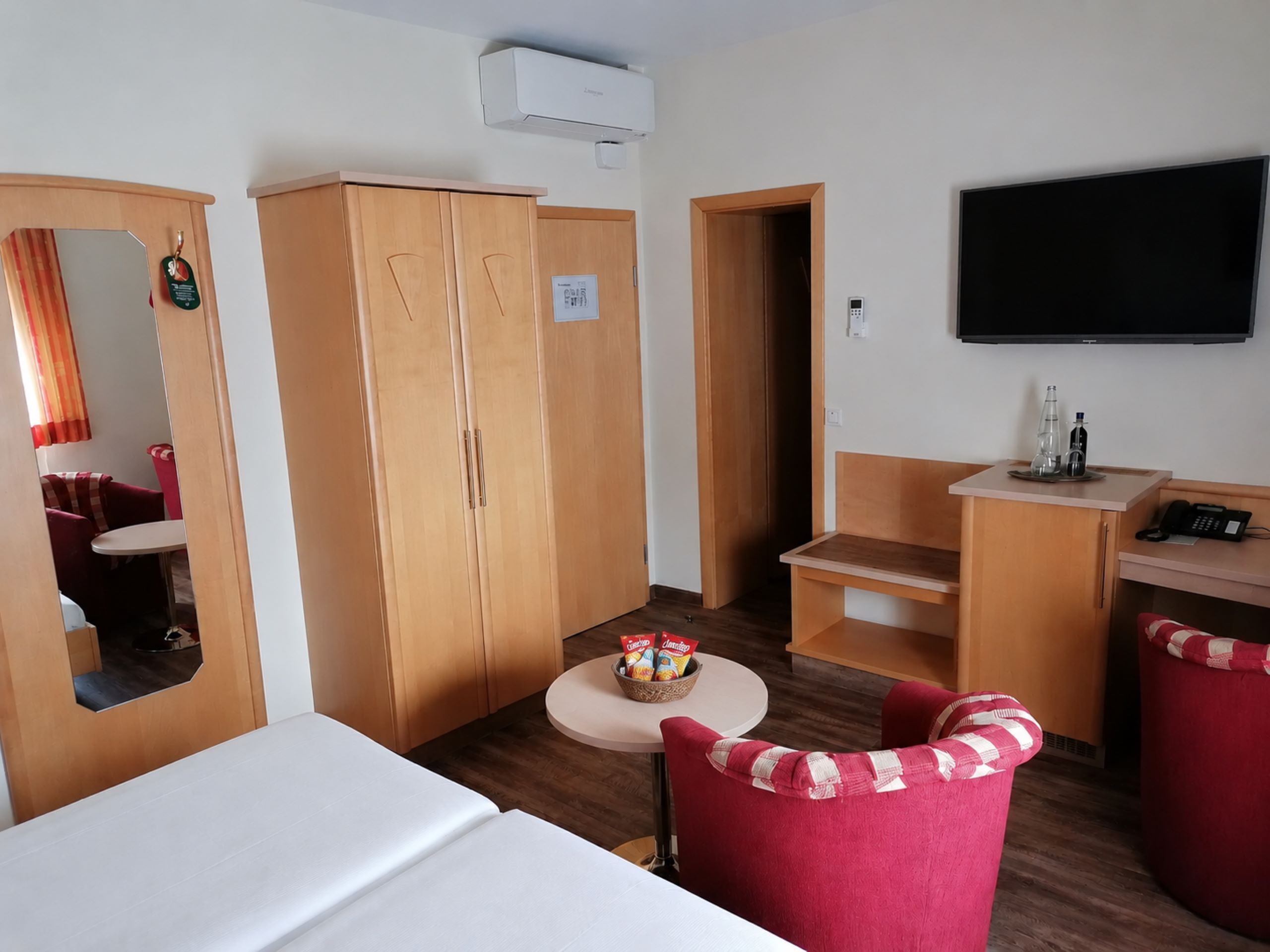 A hotel room with a bed, a desk, a chair, a television, and a wardrobe.