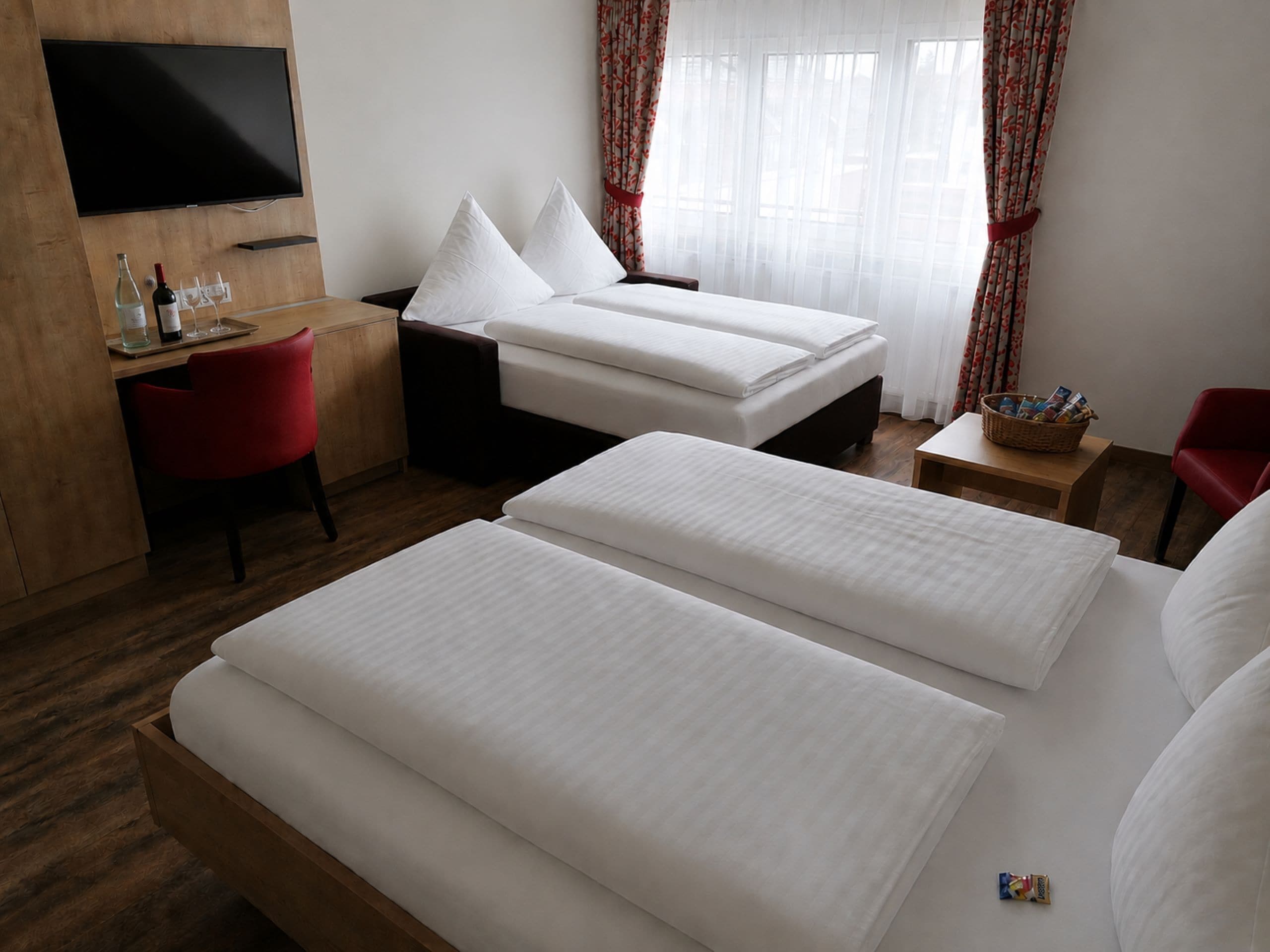 A hotel room with two beds, a desk, a TV, and a window with curtains.