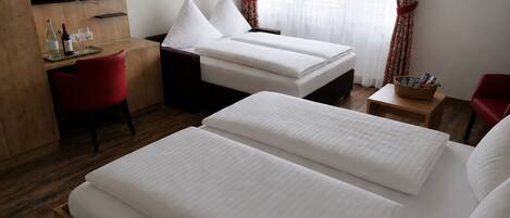 A hotel room with two beds, a desk, a TV, and a window with curtains.