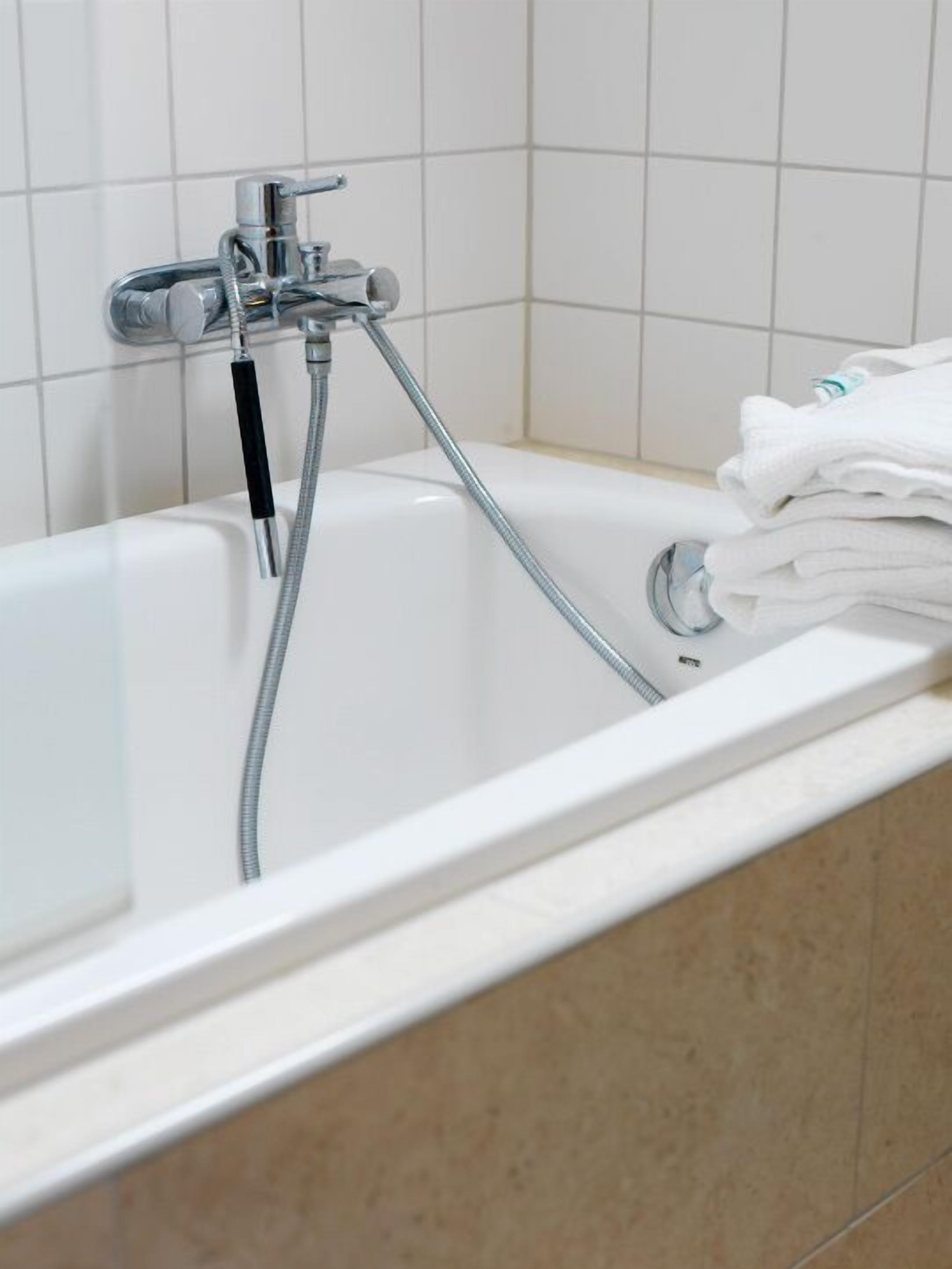 Una bañera blanca con un cabezal de ducha manual y una pila de toallas.