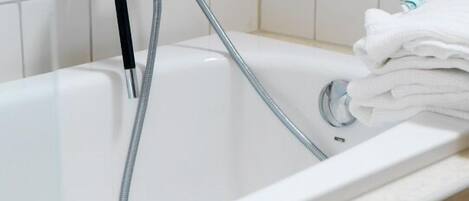 Una bañera blanca con un cabezal de ducha manual y una pila de toallas.