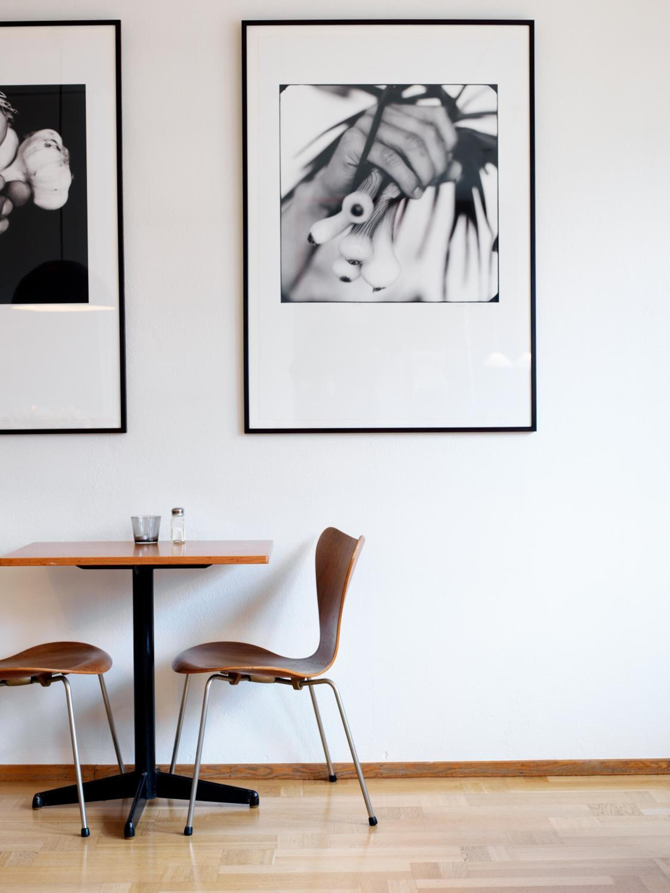 Un coin repas avec une table et deux chaises, des photographies en noir et blanc encadrées au mur et un plancher en bois.