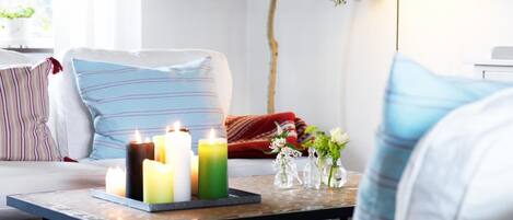 A cozy living room with a sofa, a coffee table with candles, a lamp, and a tree.