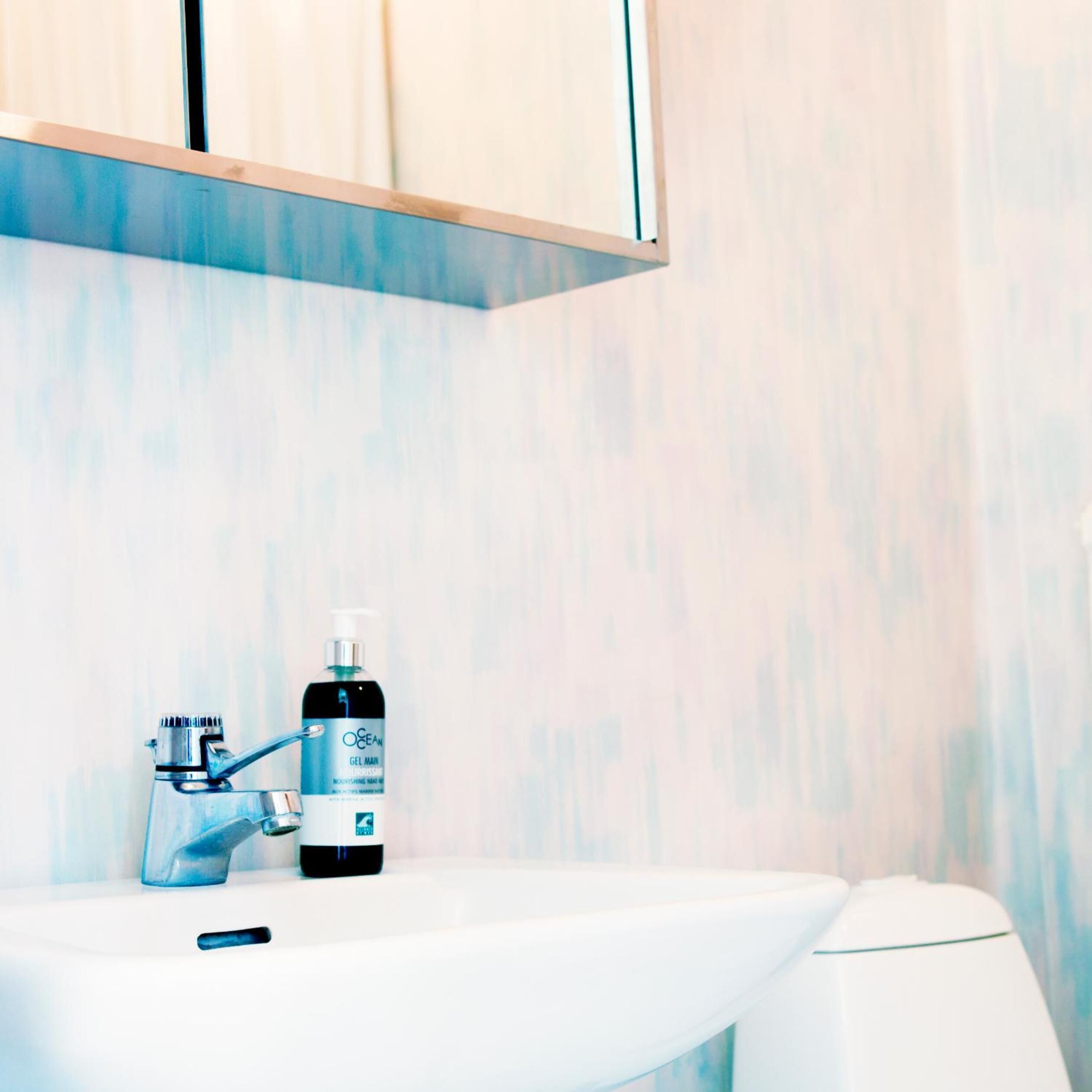 A bathroom with a white sink, a faucet, and a bottle of Ocean Gel Main on the counter.