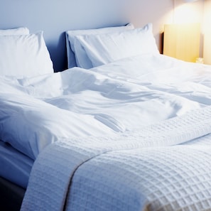 A neatly made bed with white linens and a quilted blanket.