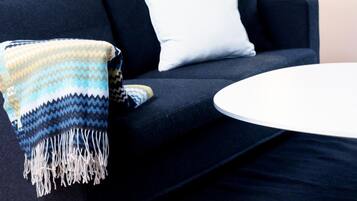 A modern living room with a dark sofa, a white pillow, a patterned throw blanket, a round white table, and a floor lamp.