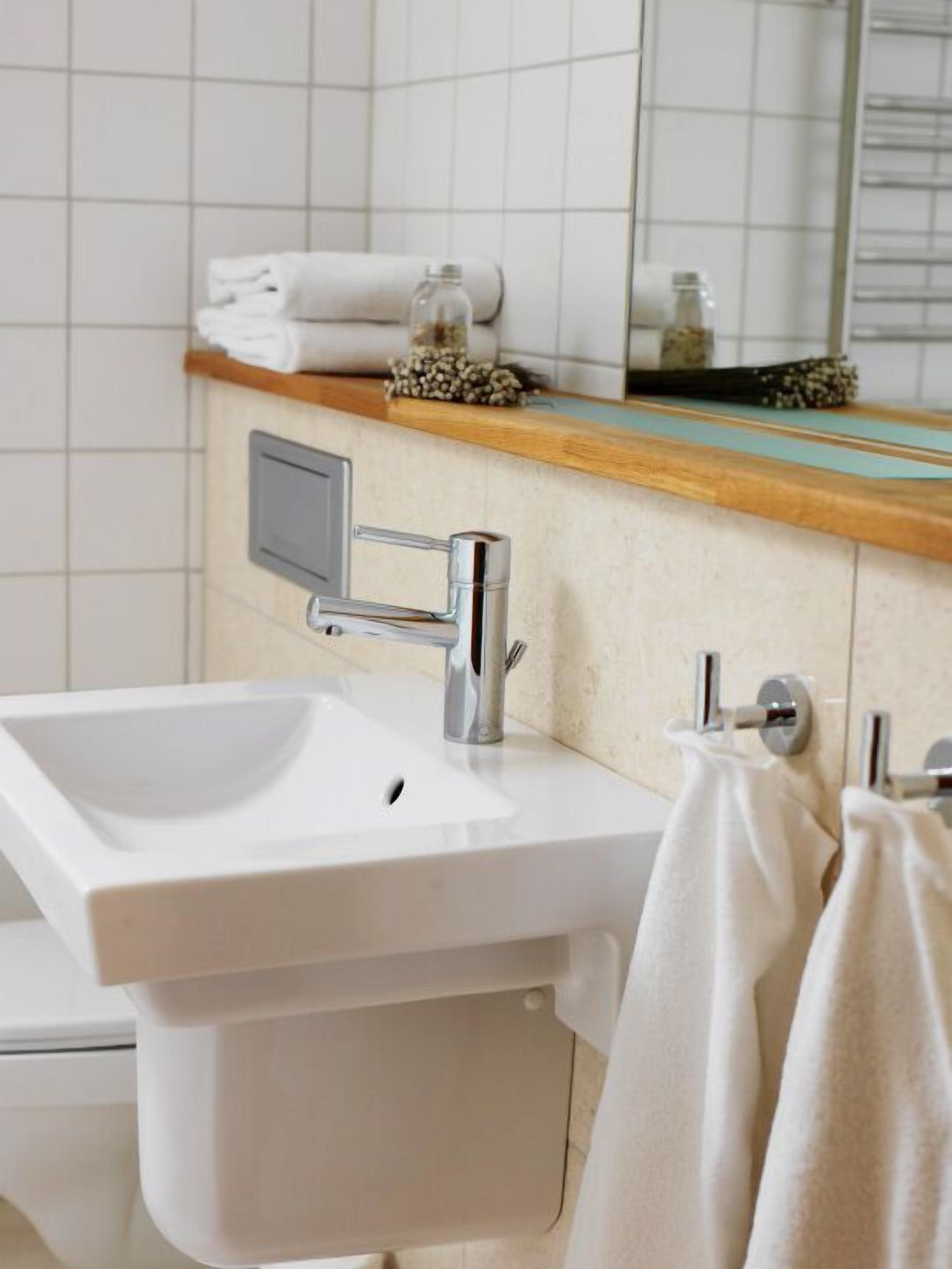 A bathroom with a white sink, chrome faucet, and a mirror above it. There is a towel rack with a towel hanging on it.