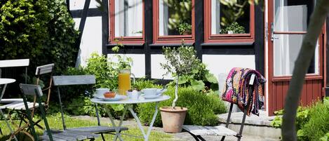 En uteplats i trädgården med ett bord, stolar och krukväxter.