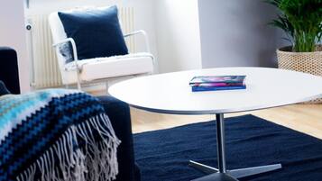 Un salón moderno con una mesa redonda blanca, un sofá azul y un amplio ventanal con plantas.