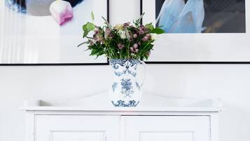 A white cabinet with two doors, a blue and white vase with flowers, and two framed pictures on the wall.