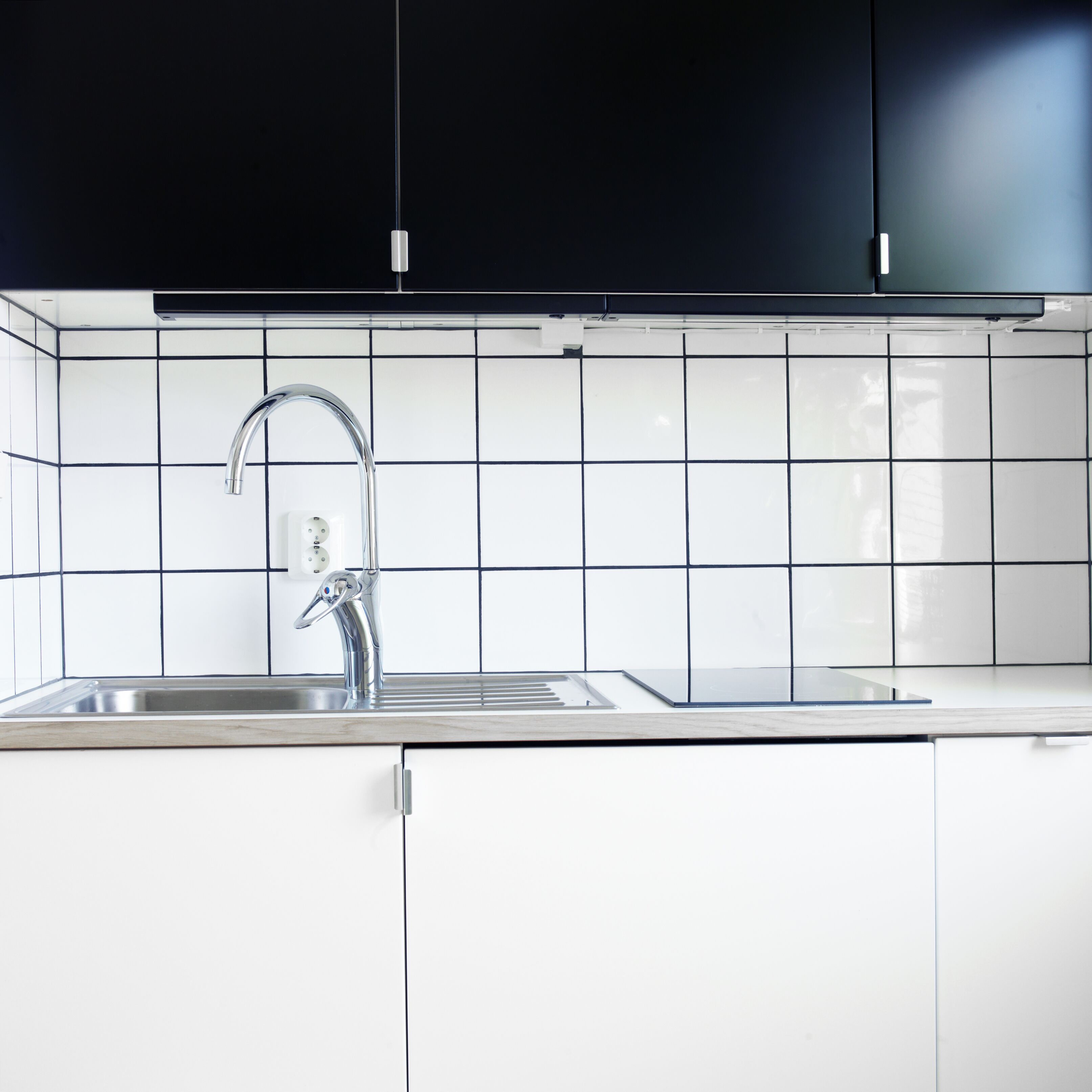 Una cocina moderna con armarios blancos, un lavamanos de acero inoxidable y un salpicadero de azulejos negros.
