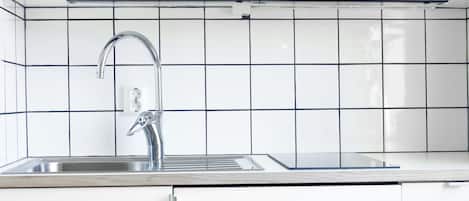 A modern kitchen with white cabinets, a stainless steel sink, and black tiled backsplash.