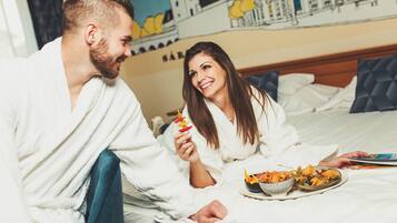 A couple in a hotel room with a bed, a breakfast tray, and a wall mural.