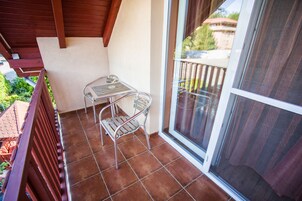 Un balcón con una mesa y sillas de metal, una puerta corredera de vidrio y vistas a un edificio y follaje.