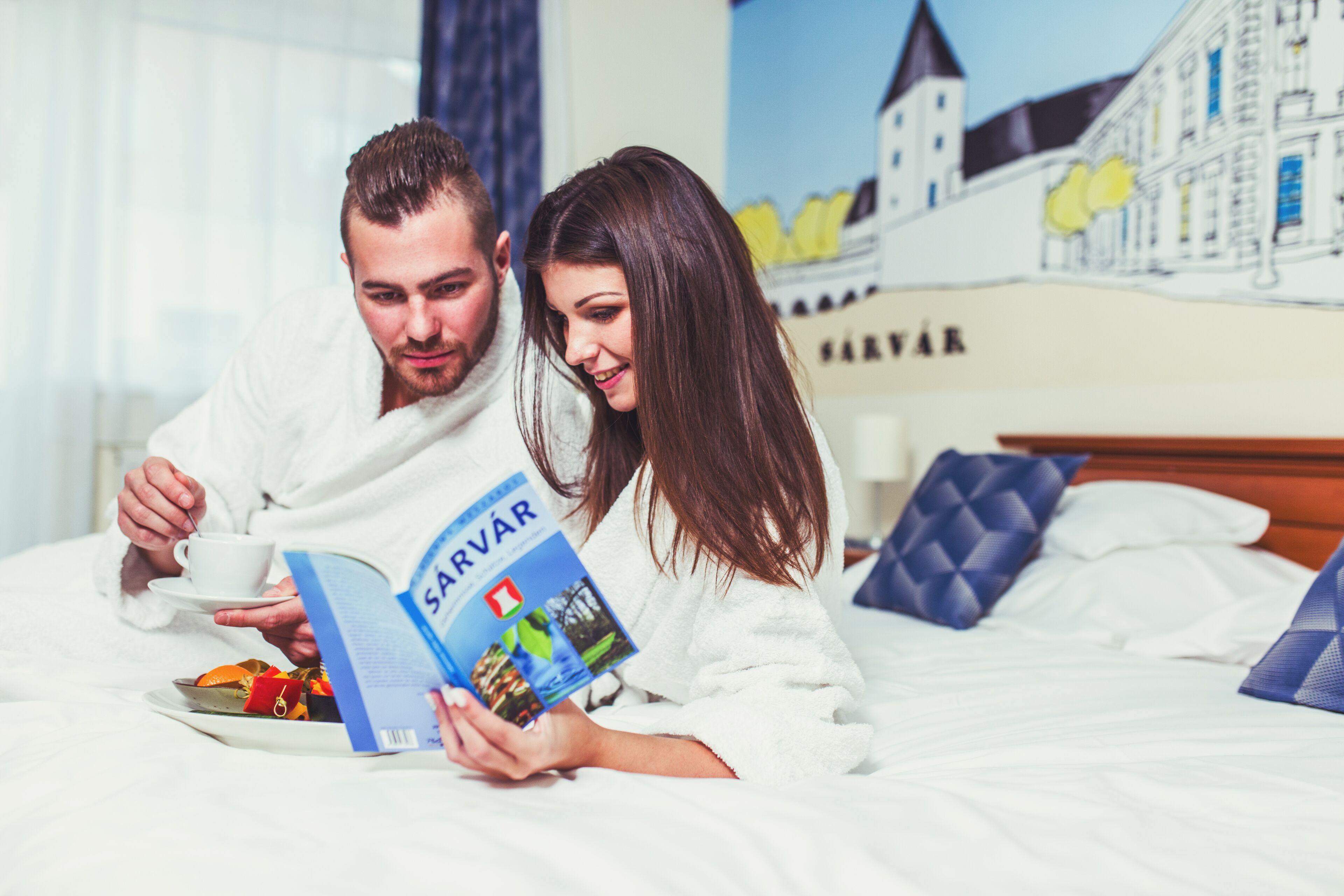 A hotel room with a bed, a book, a cup, and a plate of food.