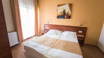 A hotel room with a large bed, a nightstand, a painting on the wall, and a window with curtains.