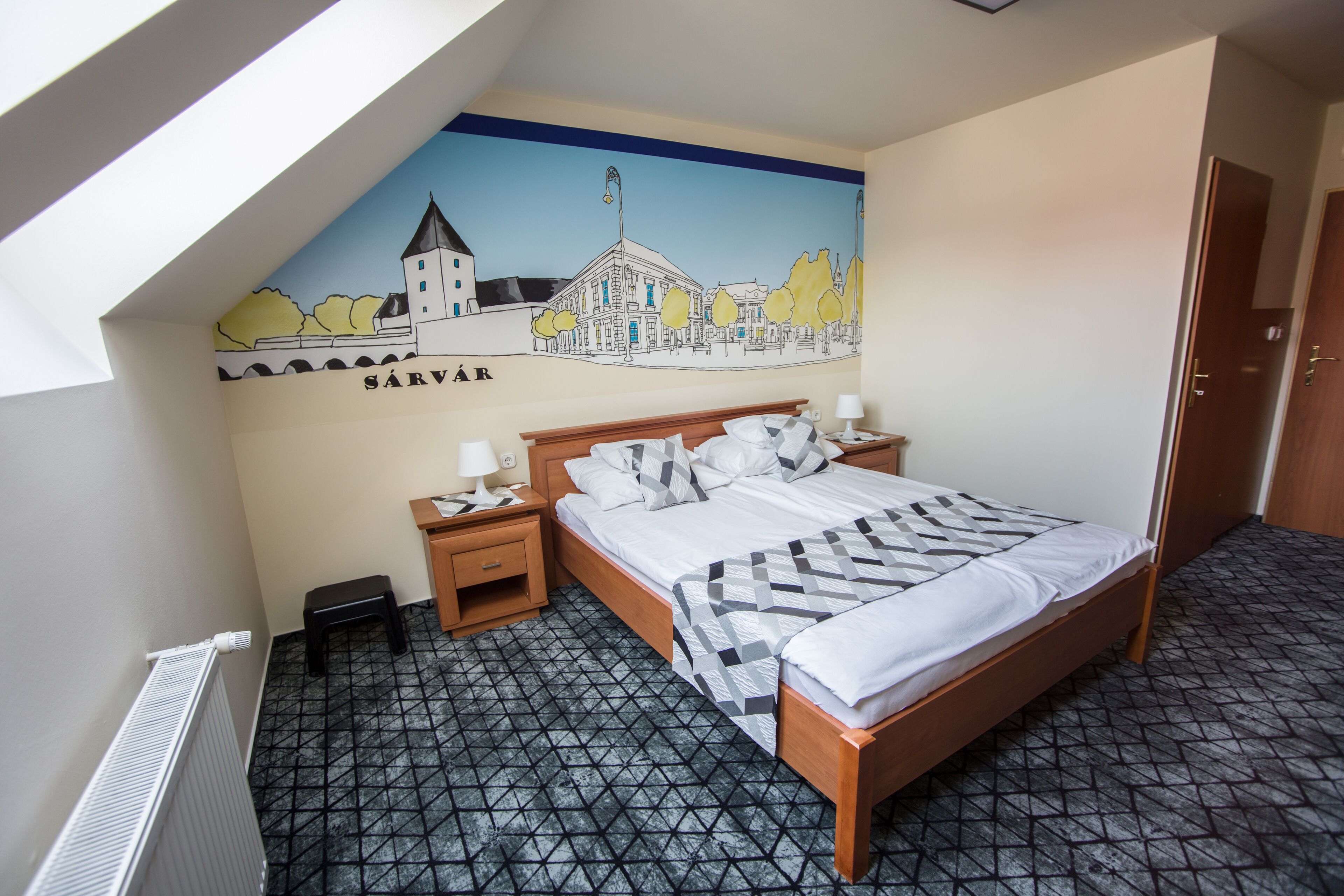 Un dormitorio con cama, mesitas de noche, un radiador, un mural en la pared y una puerta.