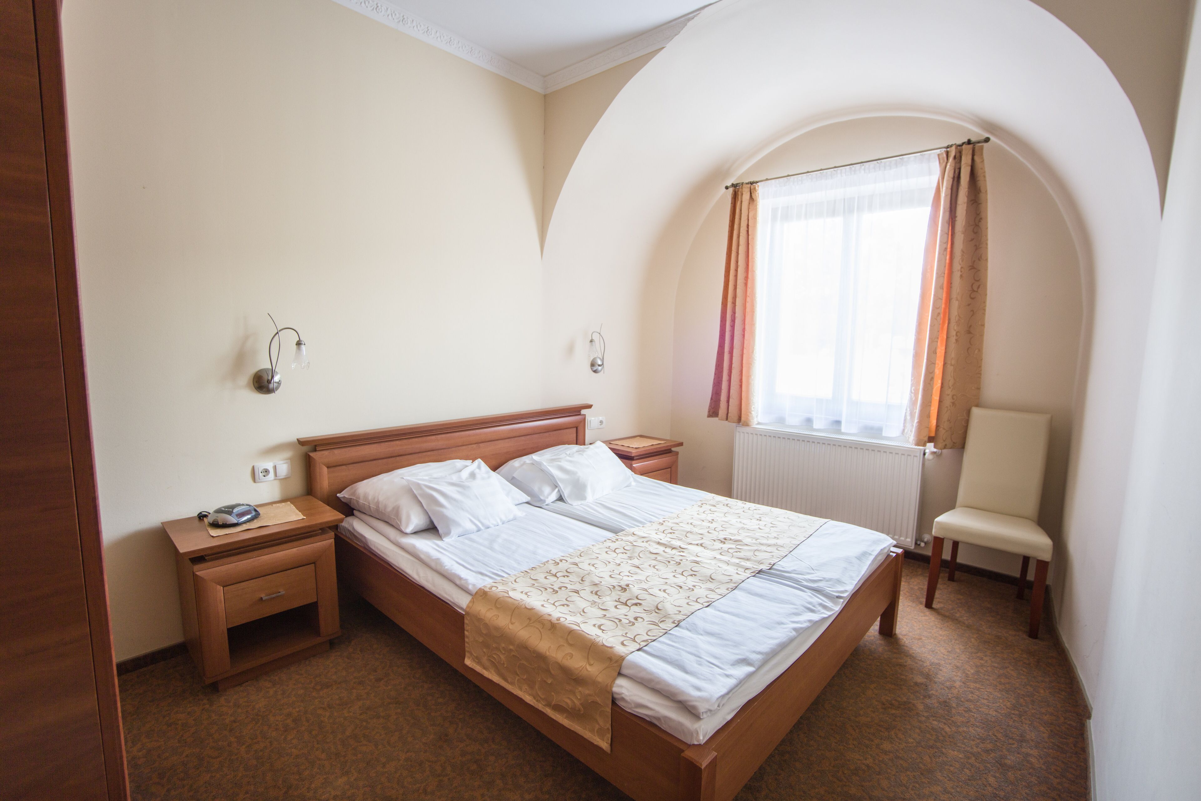 Un dormitorio con cama de madera, una mesita de noche, una silla y una ventana con cortinas.