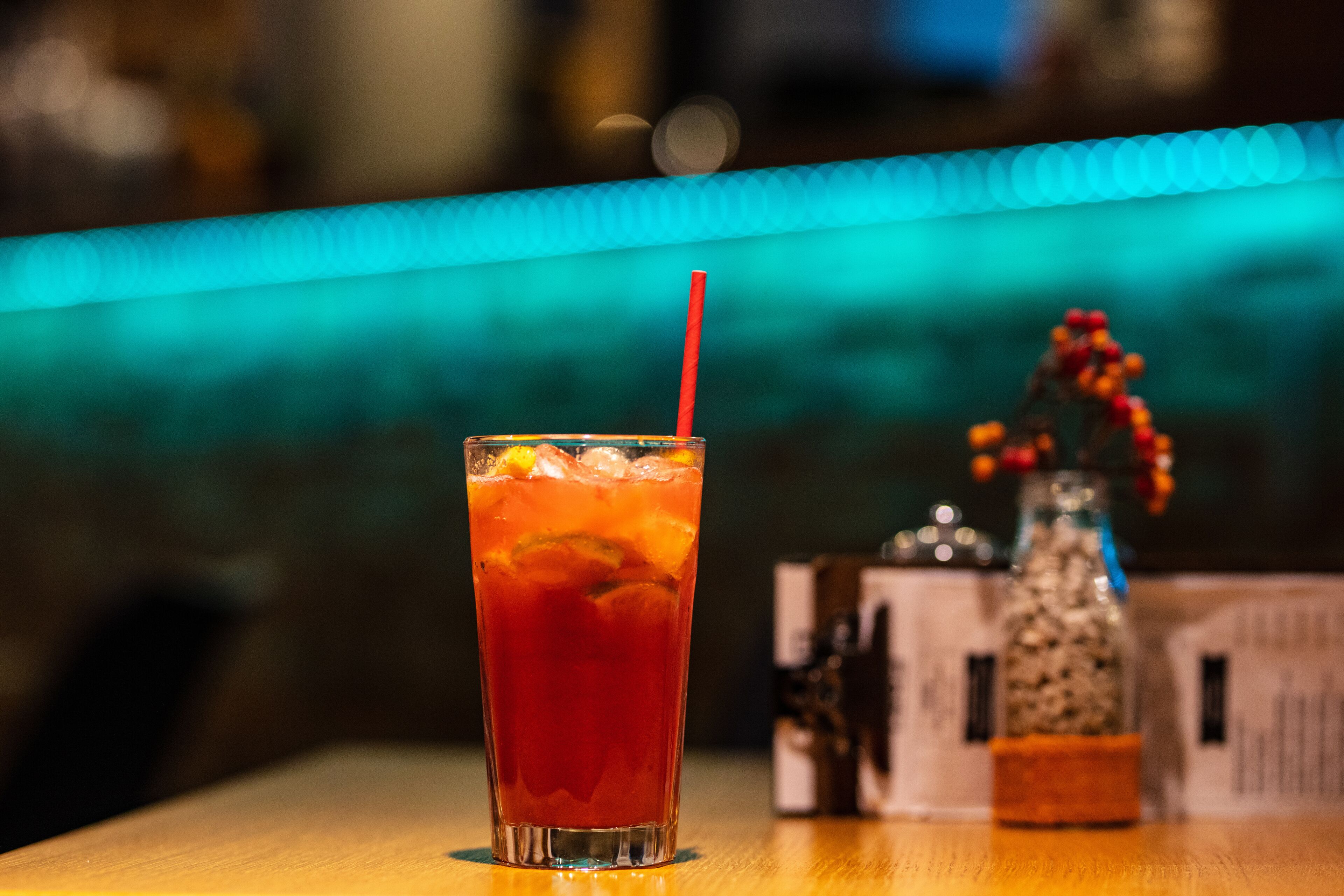 Een hoog glas met een rode rietje, gevuld met een rood drankje, op een houten tafel.