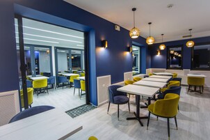 Un comedor moderno con mesas y sillas, un área de cocina a la vista y un amplio ventanal que proporciona luz natural.