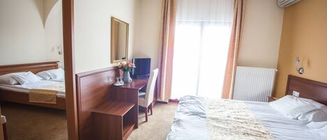 A hotel room with two beds, a desk, a chair, a mirror, and an air conditioning unit.
