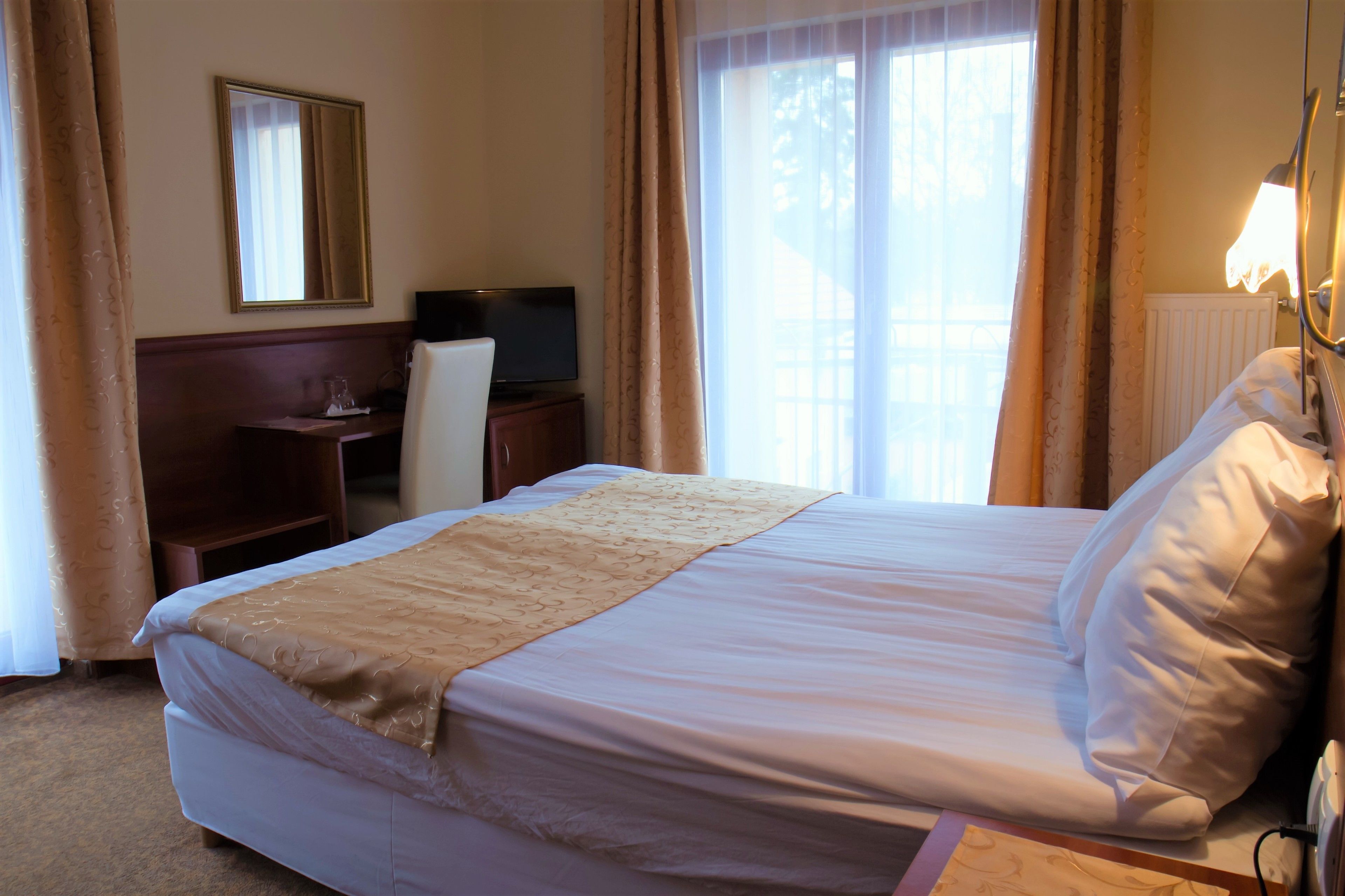 Une chambre d’hôtel avec un grand lit, un bureau avec une télévision et une fenêtre avec des rideaux.