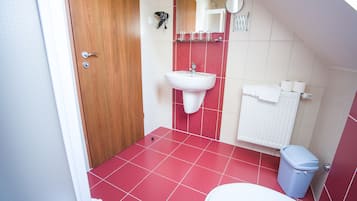 Une petite salle de bain avec une porte en bois, un lavabo blanc, des carreaux rouges, des toilettes blanches et une poubelle.