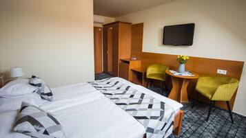 Habitación de hotel con cama, escritorio, dos sillas, televisor y una mesita con un jarrón de flores.