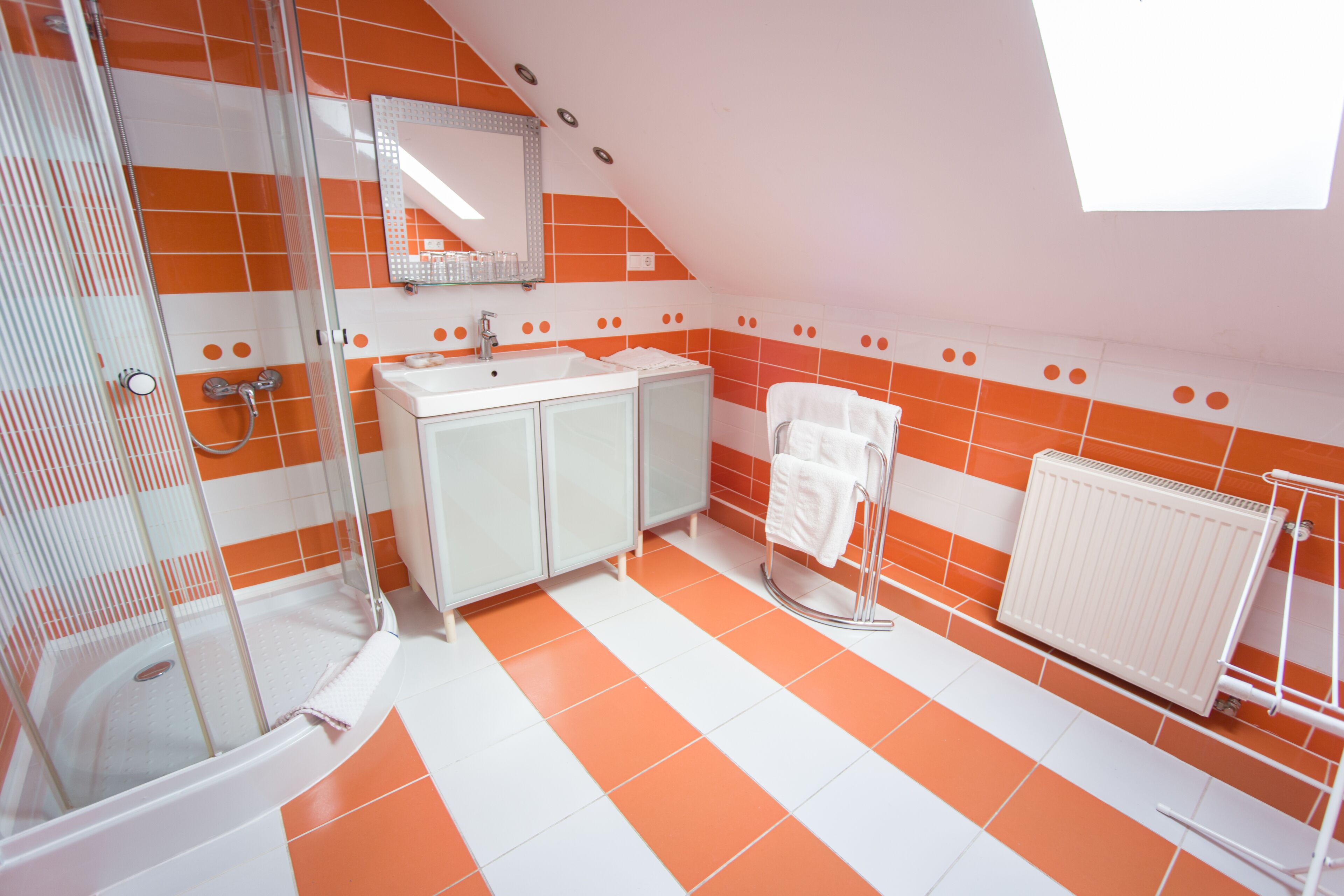 Une salle de bain avec des carreaux orange et blancs, une douche en verre, un lavabo blanc et un porte-serviettes.