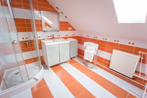 Un baño con azulejos anaranjados y blancos, cerramiento de ducha de vidrio, lavamanos blanco y un perchero para toallas.